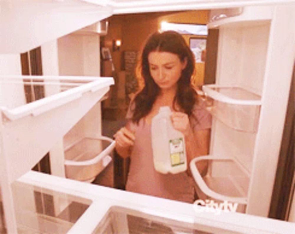 a woman is holding a gallon of milk in front of an empty refrigerator that says city