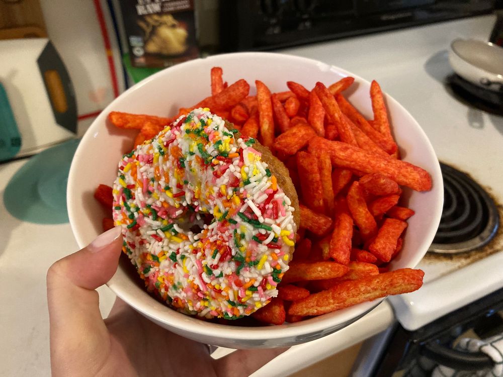 a soup bowl completely filled with chester’s hot fries and a sprinkle donut sitting on top. 