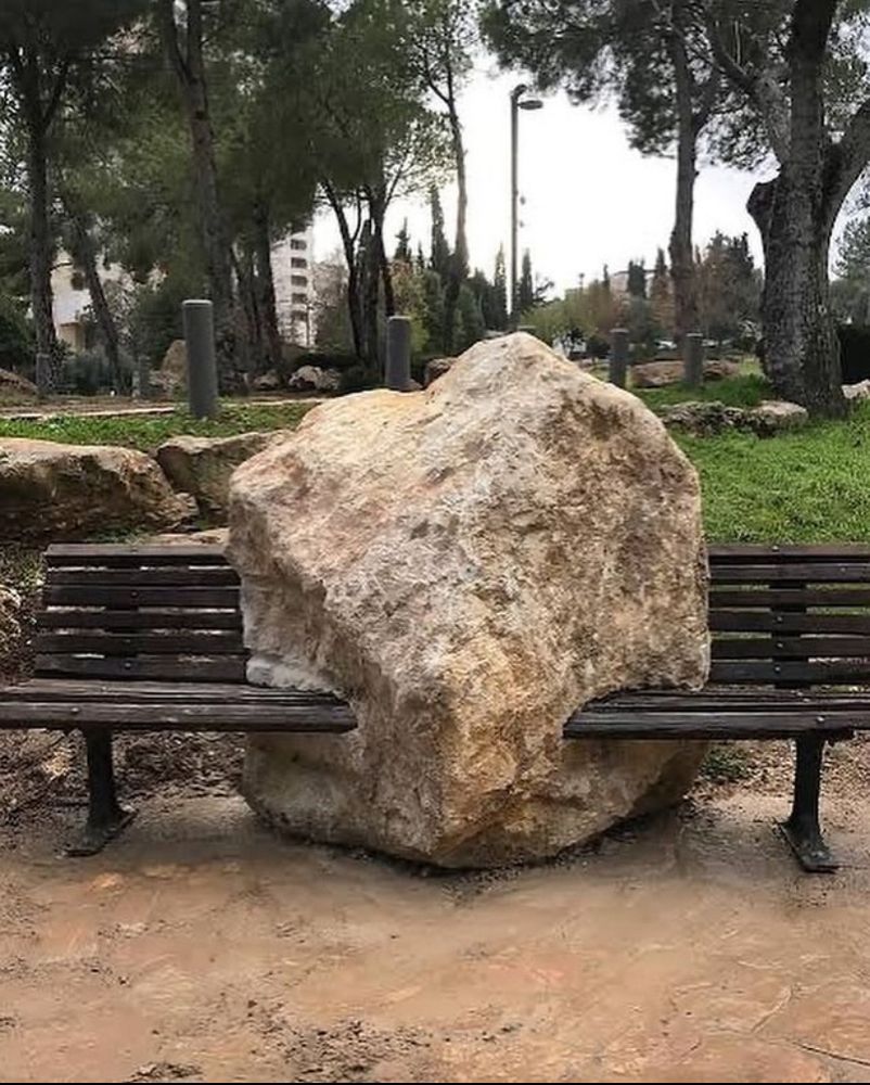a park bench with into a boulder embedded into the middle of it 