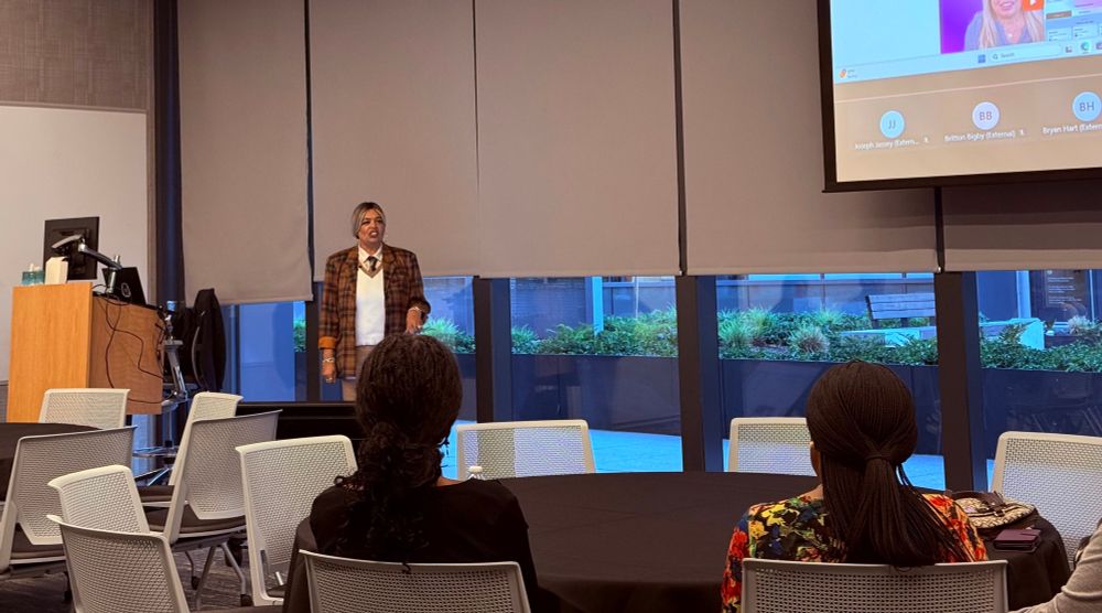 Karuana standing near a podium in front of an audience with a projection screen behind her in Microsoft’s Redmond headquarters 