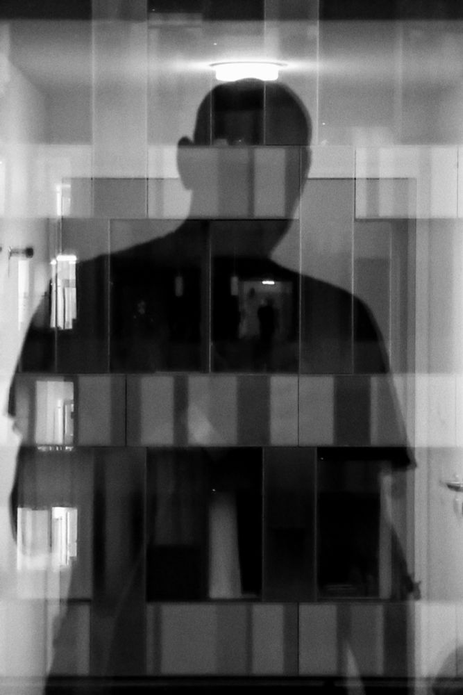 A persons silhouette reflected in a window, other rooms visible on the other side. Within the figure a person stands in a lot room where the heart would roughly be