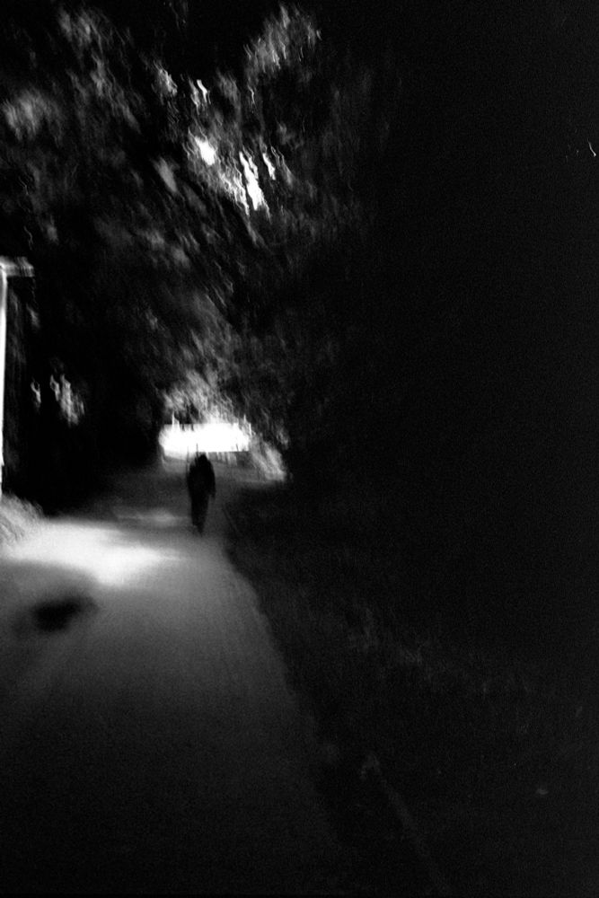 A blurry figure stands on a path besides a brighter area. A tunnel like light in the background