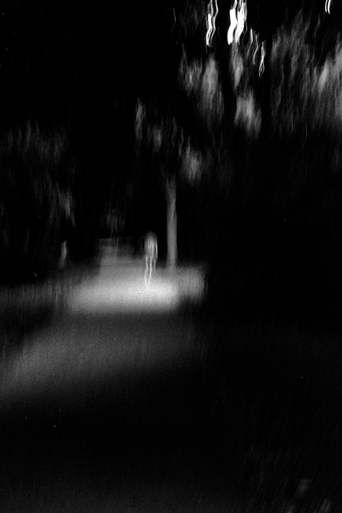 A blurry figure standing in a lit patch of a dark path 
