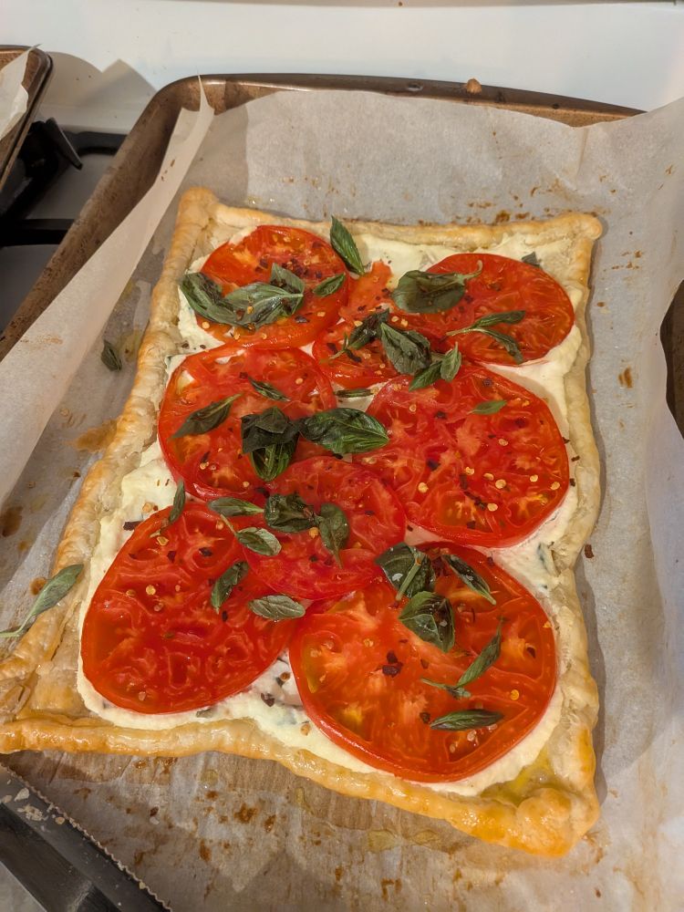 a photo of a tomato tart topped with basil on a parchment lined baking sheet