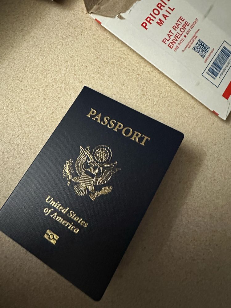 A brand new US passport that says “passport United States of America” with an emblem of an eagle in gold type.
