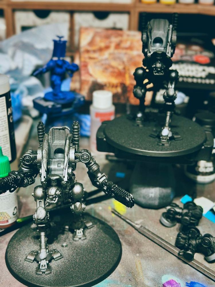 Two detailed robot figures stand on their bases, appearing partially painted in black primer...