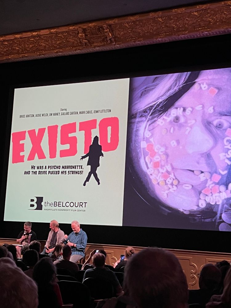 The writers of Existo are interviewed at the Belcourt Theatre after a screening. Behind them is a huge splash of Existo drowning in alphabet soup.