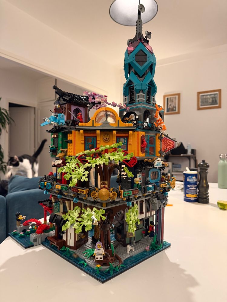 Un set de lego monté avec au premier plan un arbre géant qui passe à travers le premier étage , pleins de couleurs et une grande tour bleue qui domine tout 
