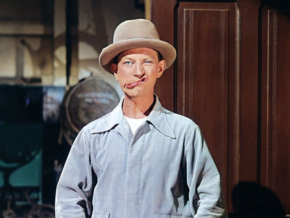 A man wearing a light grey jumpsuit and a beige fedora is making a very silly face at the camera. Donald O'Connor, born on this day in 1925 (d. 2003) as Cosmo Brown in a scene from the film SINGIN' IN THE RAIN (1952) Tags Filmsky moviesky MOVIES films botd happy birthday Hollywood legends star actor comedy slapstick MGM musical classic 