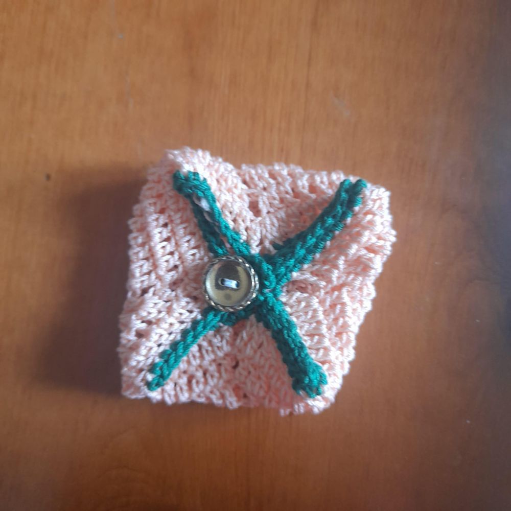 Un porta cuffiette quadrato fatto all'uncinetto, colore arancione e verde, chiuso da un bottoncino dorato