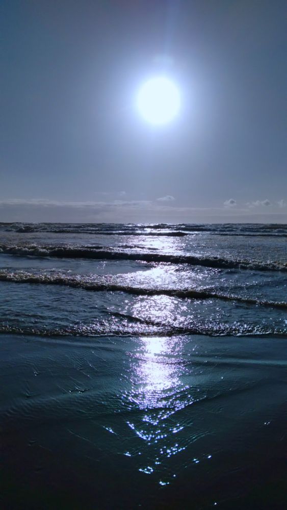 sun setting and reflecting on pacific ocean waves with faint cloudless blue skies