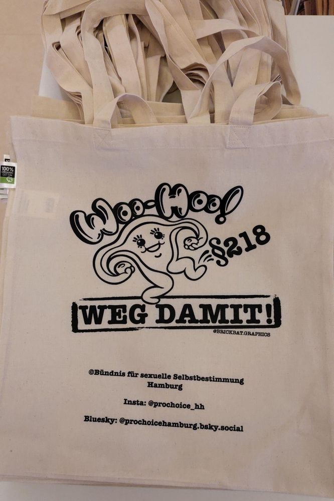 Ein kleiner Stapel Jutebutel liegt auf einem Tisch. Der oberste ist zu sehen. Er ist naturfarben, auf den Beutel aufgedruckt ist Ute, ein Comic-Uterus, der den Paragraphen 218 wegschießt. Darüber steht: Woo-Hoo! Und darunter: Weg damit!
Darunter wiederum steht: @brickbat.graphics
Und dann: © Bündnis für sexuelle Selbstbestimmung Hamburg 
Darunter dann die Handles unseres Insta- und unseres Blueskyaccounts.