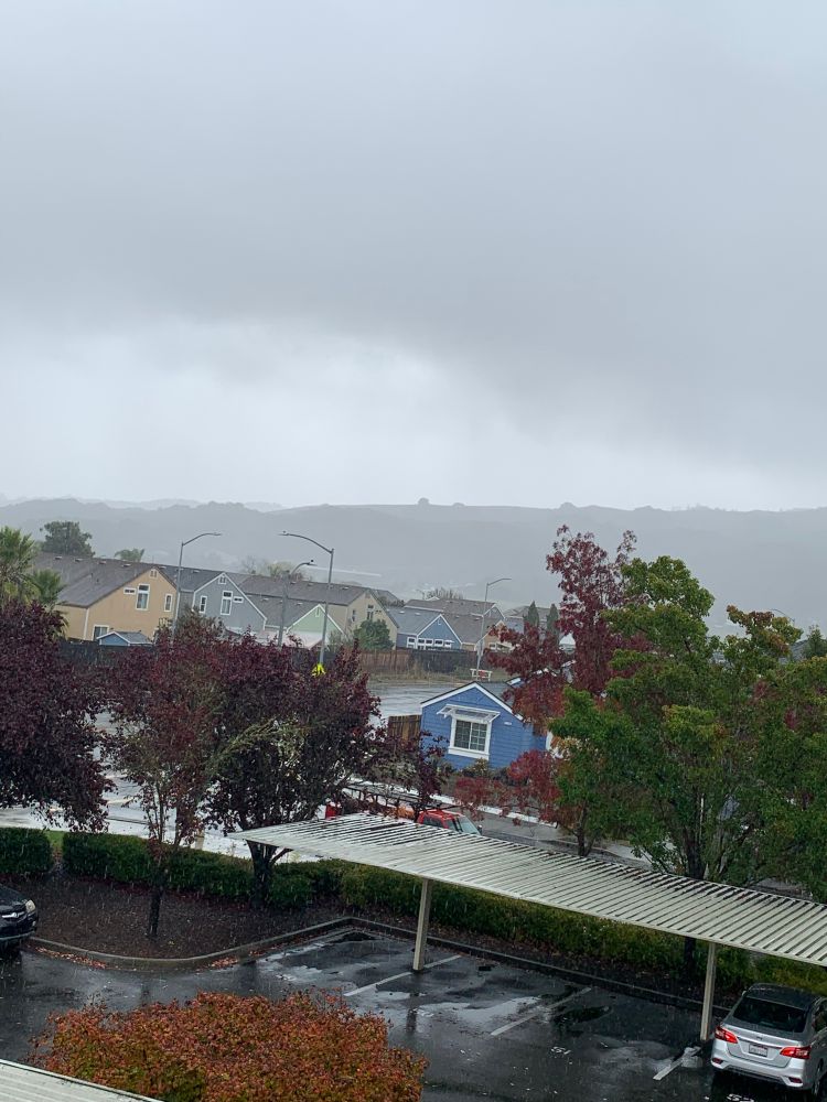 Gray, misty skies from the rain we’ve gotten; the hillsides are slightly hidden by the mist and there are houses and trees nearby 