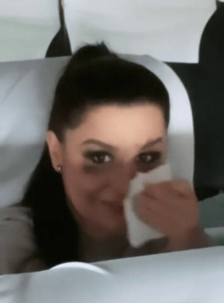 a woman wipes her nose with a napkin while sitting on a plane