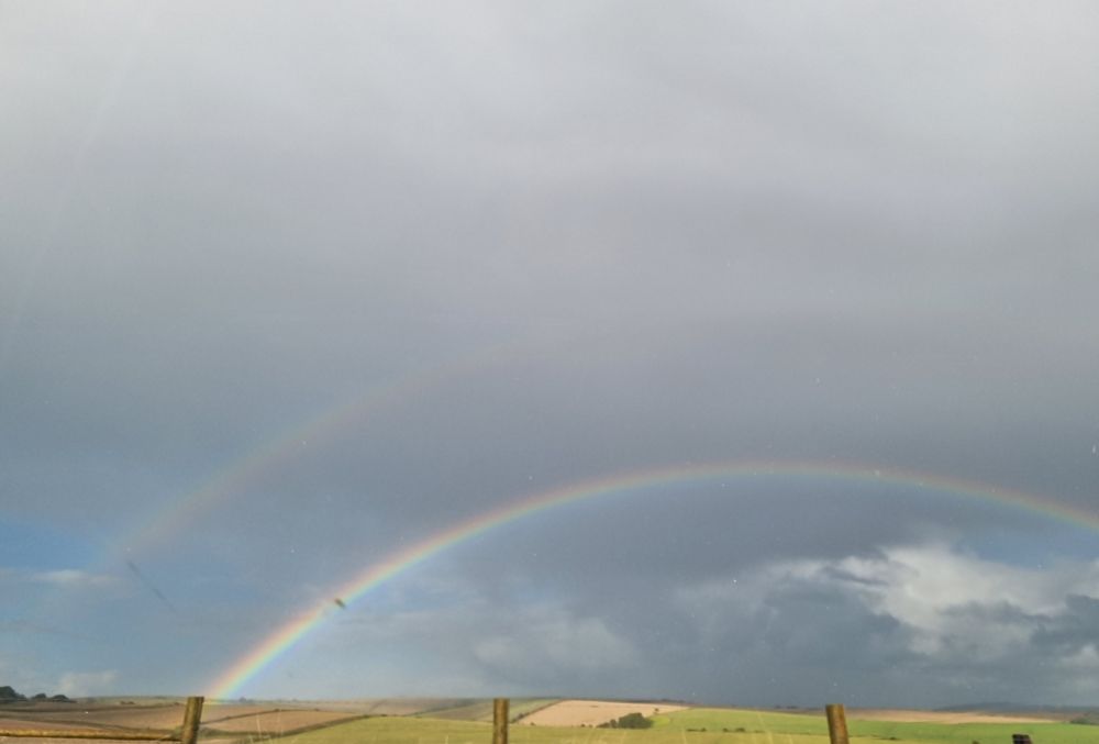 A double rainbow in grey skies above green fields. 