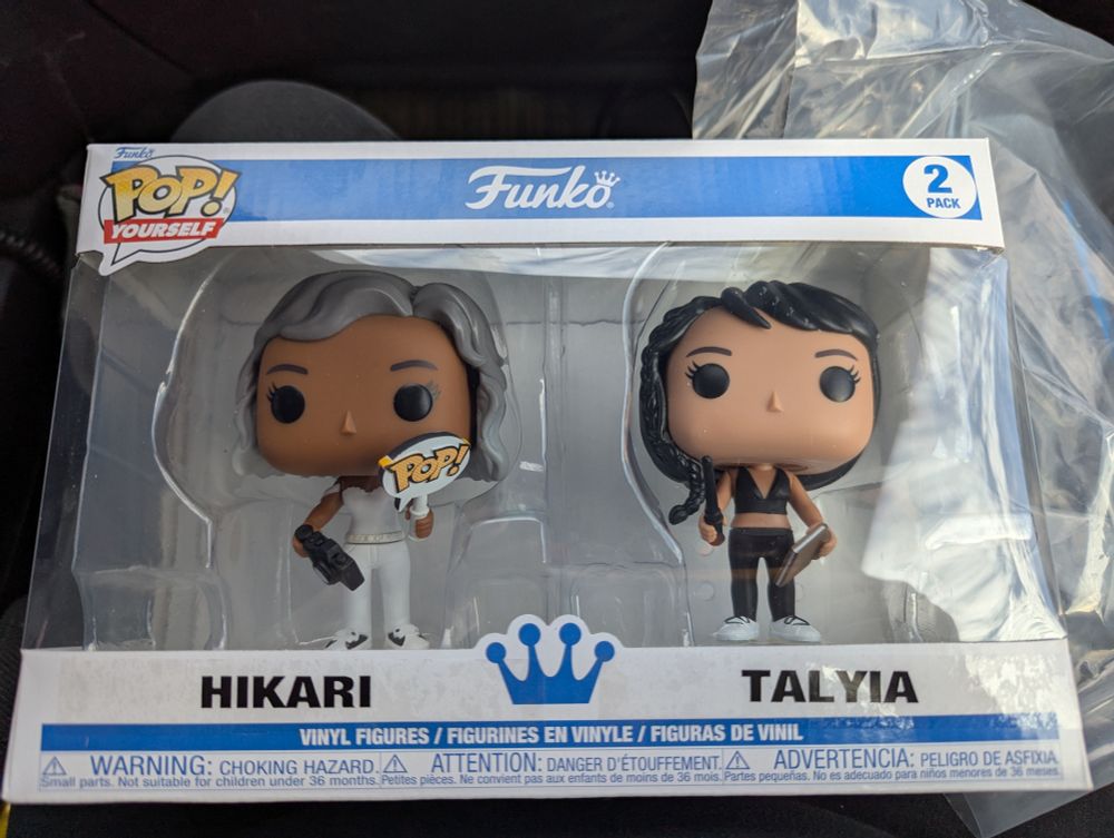 Hikari (white hair and outfit with camera and POP sign) and Talyia (black hair and outfit with book and baton)