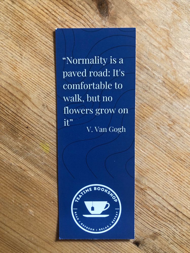 A blue card bookmark from the TeaTime Bookshop. Their logo is at the bottom and above is printed “Normality is a paved road: It’s comfortable to walk, but no flowers grow on it”.