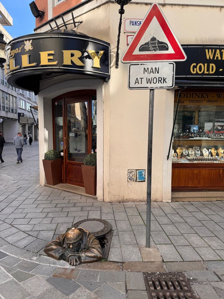A bronze statue of a sewer worker coming out of a man hole cover in the street. 