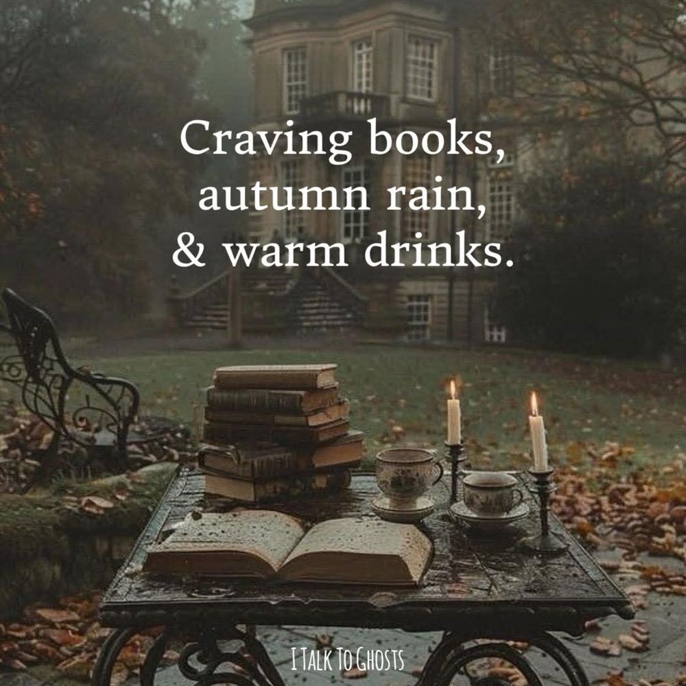 Moody, misty scene with fallen leaves on the ground. There's a wrought iron patio table with taper candles burning, and a stack of books, in front of a Gothic home and large, partially bare trees. White text overlay says "Craving books, autumn rain, & warm drinks."