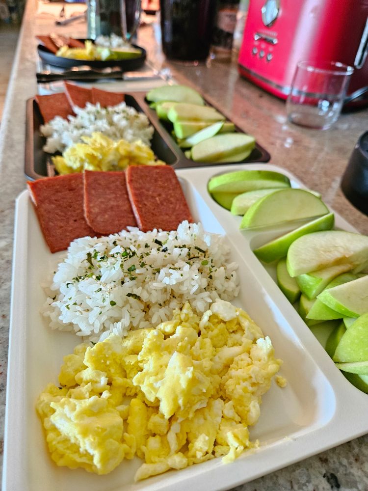 Several sectioned plates, each containing: eggs, rice with furikake, spam, and apple slices. 