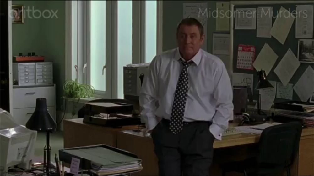 a man in a white shirt and tie stands in front of a bulletin board with midsomer murders on it