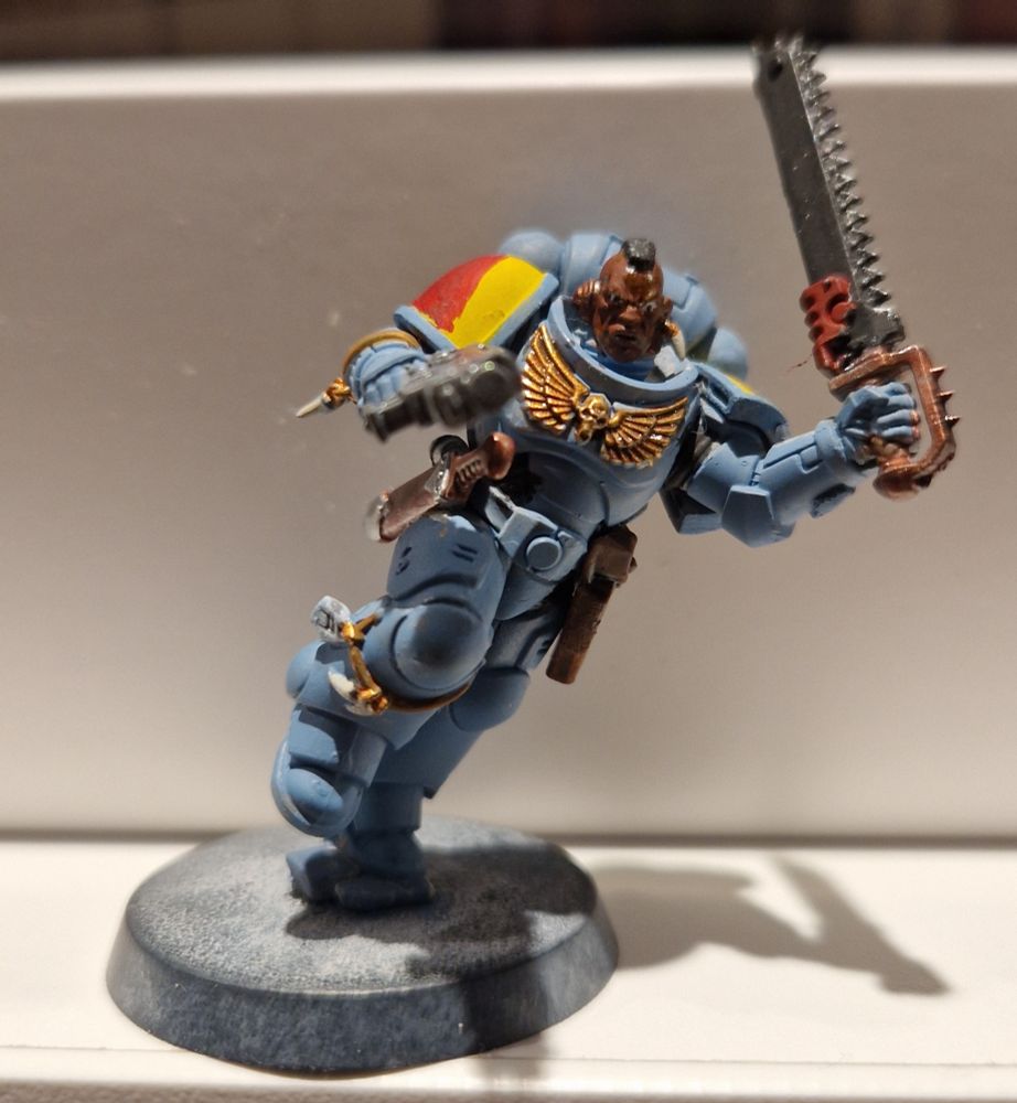 Figurine de griffe sanglantebtête nue à la peau noire avec une coiffure de type mohawk, un pistolet bolter et une épée tronçonneuse.