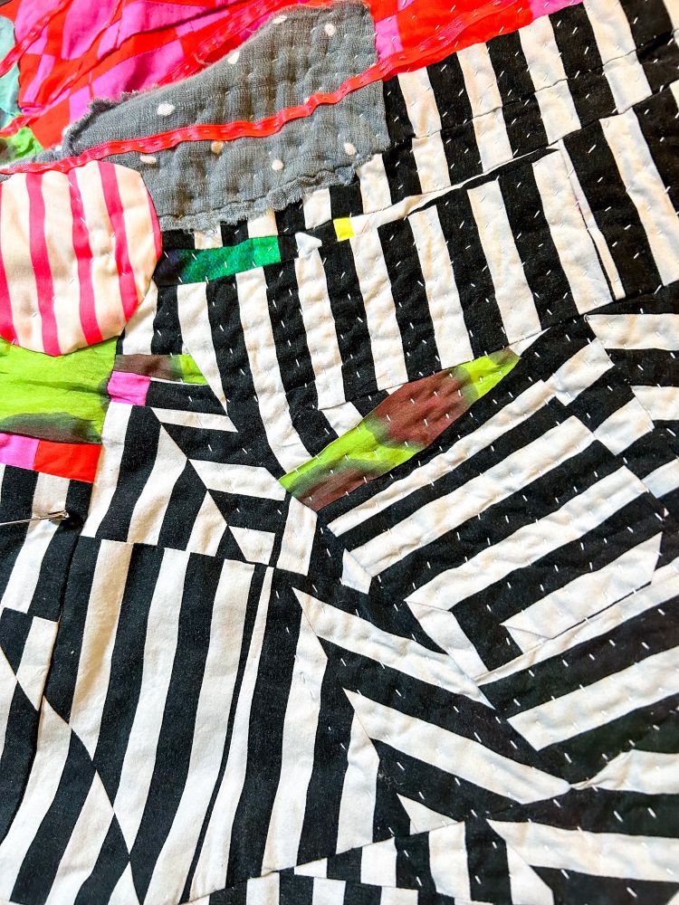 Detail view of stripe quilt top with white thread hand stitches. 