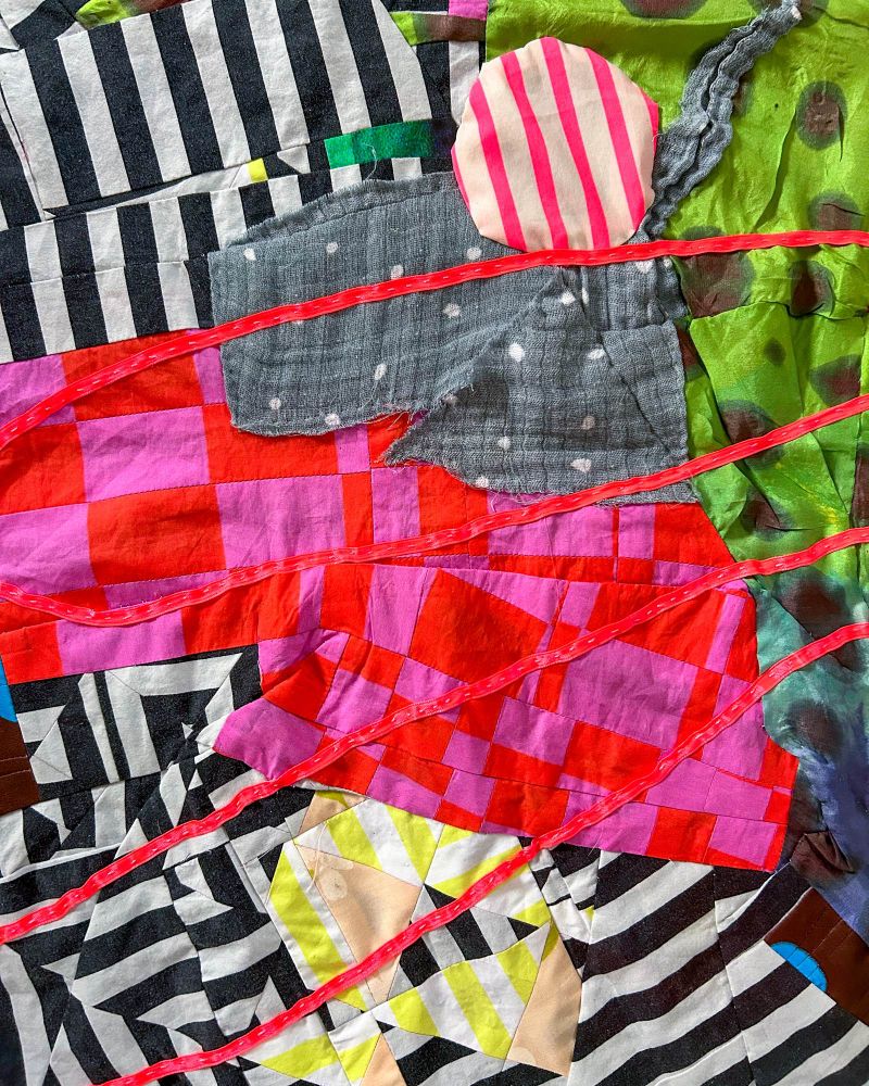 Detail of an abstract quilt top with black and white stripes, hot pink checks, neon pink ribbon and pink and white stripe circle. 