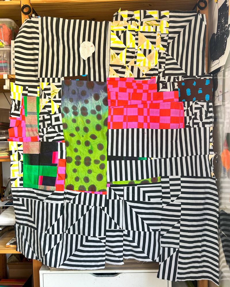 Abstract working quilt top hanging from wood shelving. 
