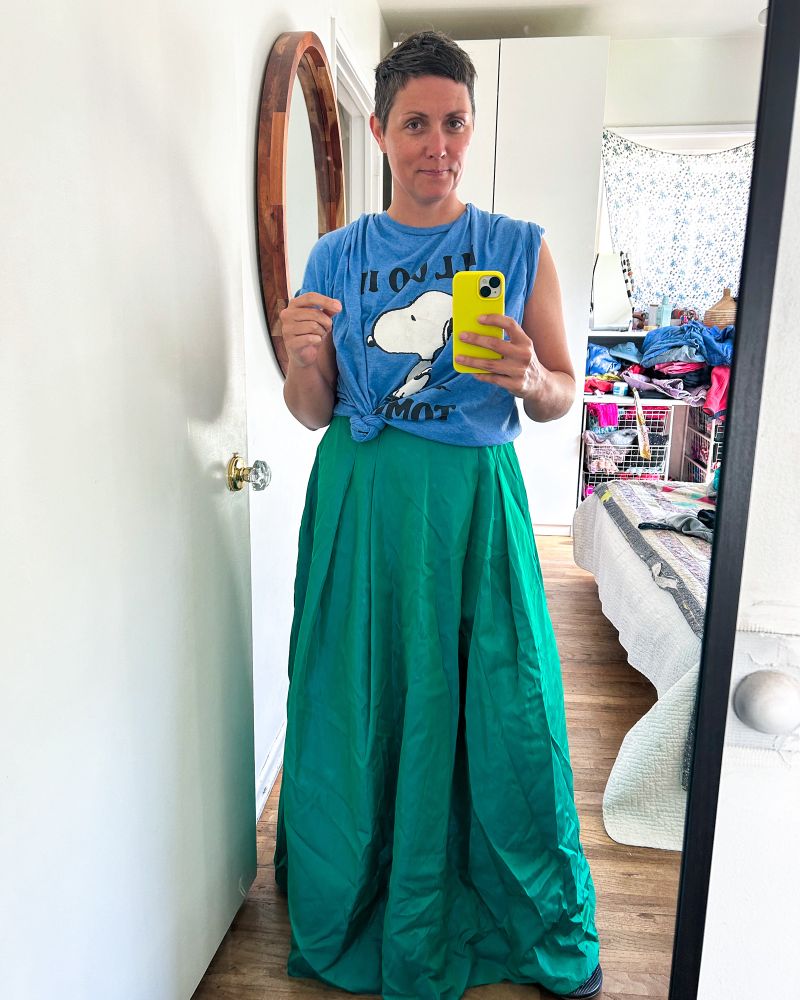 Angie’s reflection in a mirror wearing a oversized blue snoopy t-shirt and floor length green skirt. 