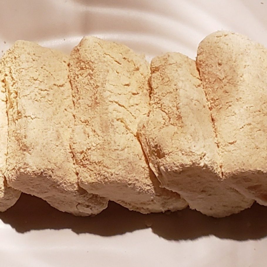 Four pieces of tan injeolmi coated with toasted soybean flour and lying slightly overlapped on a white plate 