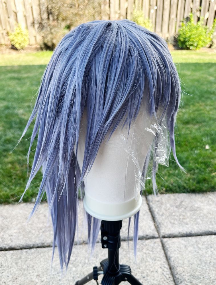 Picture of a silvery blue wig on a wig tripod cut and styled to look like Riku’s hair from KH2