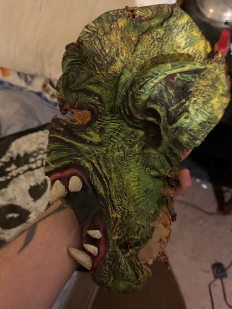 The left side of a green monster mask with pointed ears and big fangs
