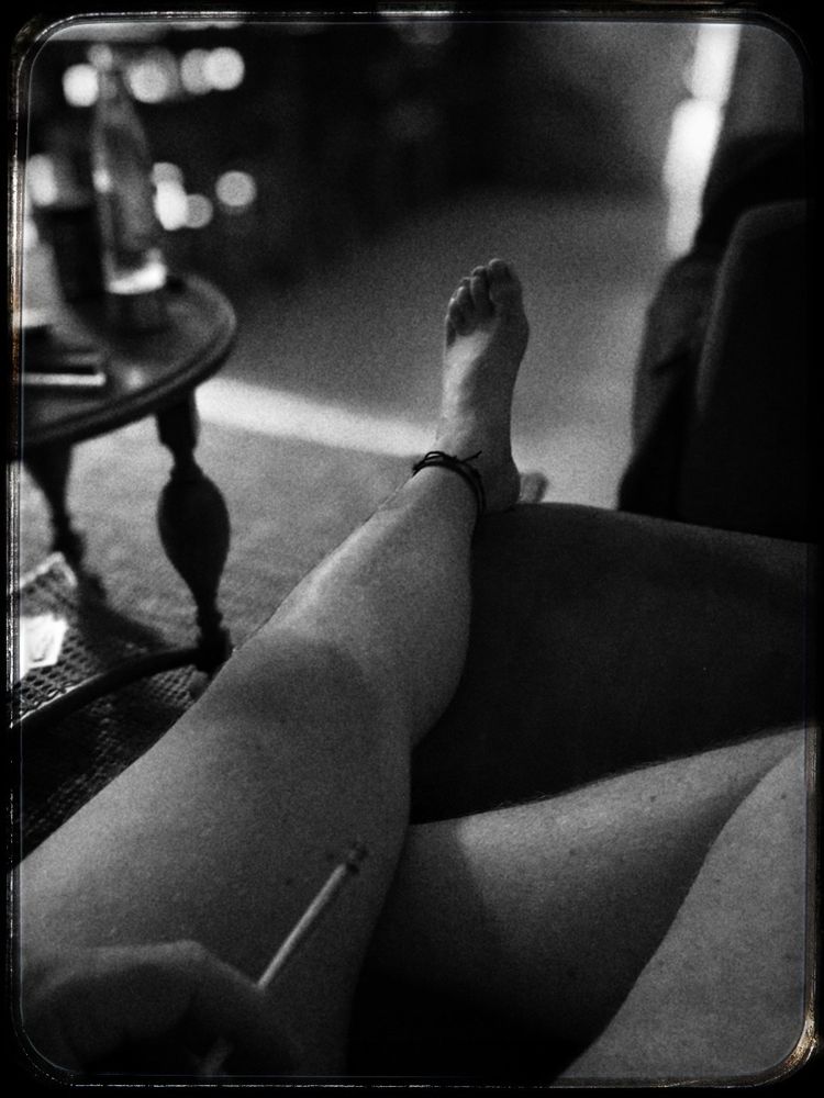 Schwarz-weiss Bild: ich sitze nackt auf dem Sofa und rauche einen Joint. Zu sehen ist ein linkes ausgestrecktes und ein rechtes angwinkeltes Bein. Der Hintergrund ist etwas blurry