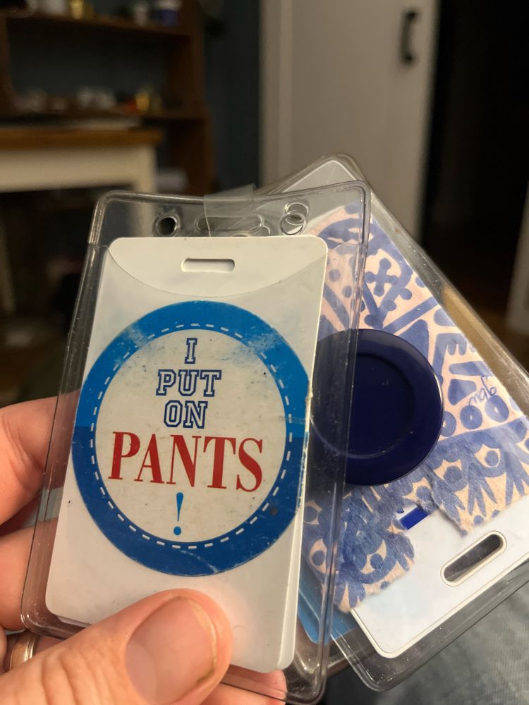 A pair of key cards on an elastic dongle. One has a post it with a doodle. The other has a round sticker that bears the words “I PUT ON PANTS !”