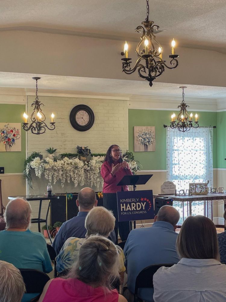 A picture of Kimberly Hardy standing a podium speaking to a group of interested-looking people. 