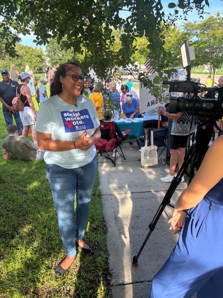 Picture of Kimberly Hardy in a "social workers vote!" t-shirt being interviewed outside with people in the background