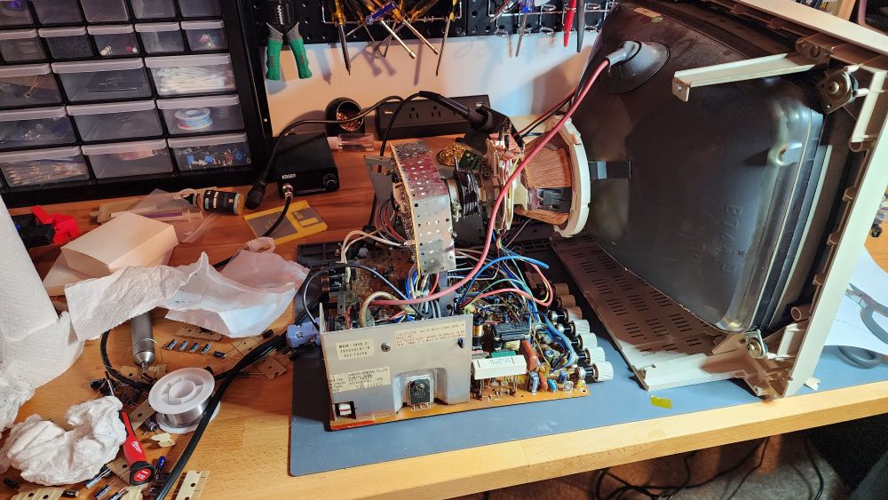 A vintage computer monitor opened up being repaired. The monitor is sitting on an electronics repair workbench