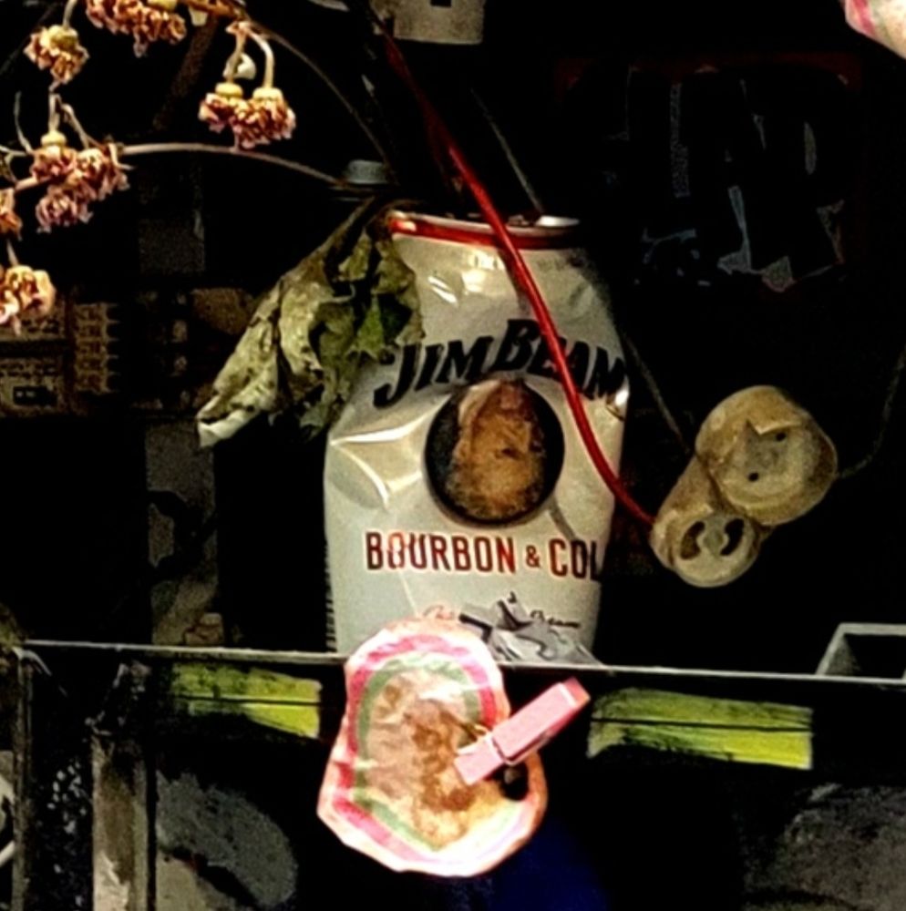 Slightly crushed Jim Beam Bourbon and Cola can inside a broken, arrow-shaped light fixture. The can has a mysterious, upside down portrait on the front. 