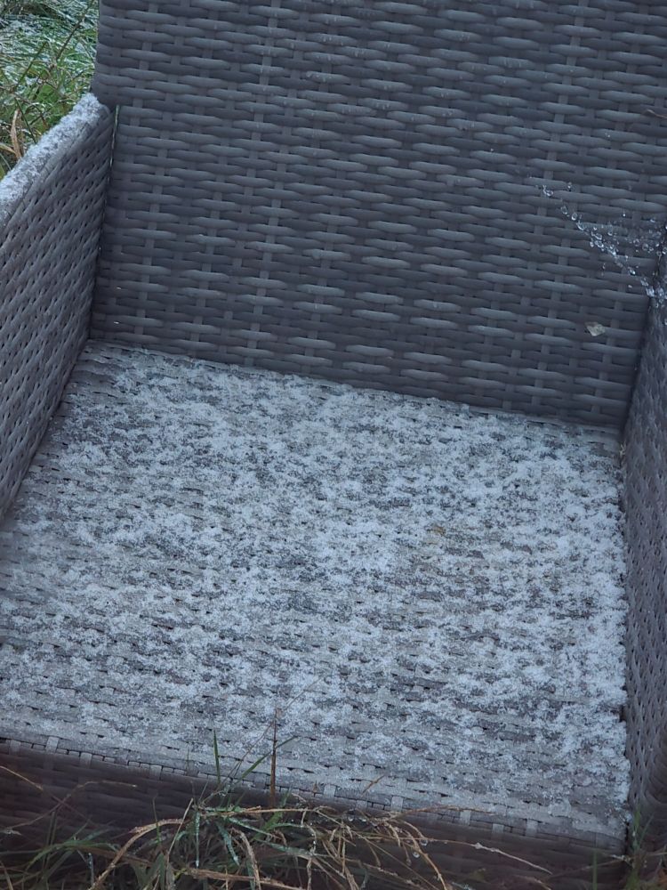 Grey rattan style garden chair covered in a very light dusting of snow