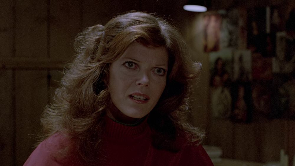 a still from The Brood (1979). a close-up of Samantha Eggar as Nola Carveth. she is wearing a red roll-neck sweater