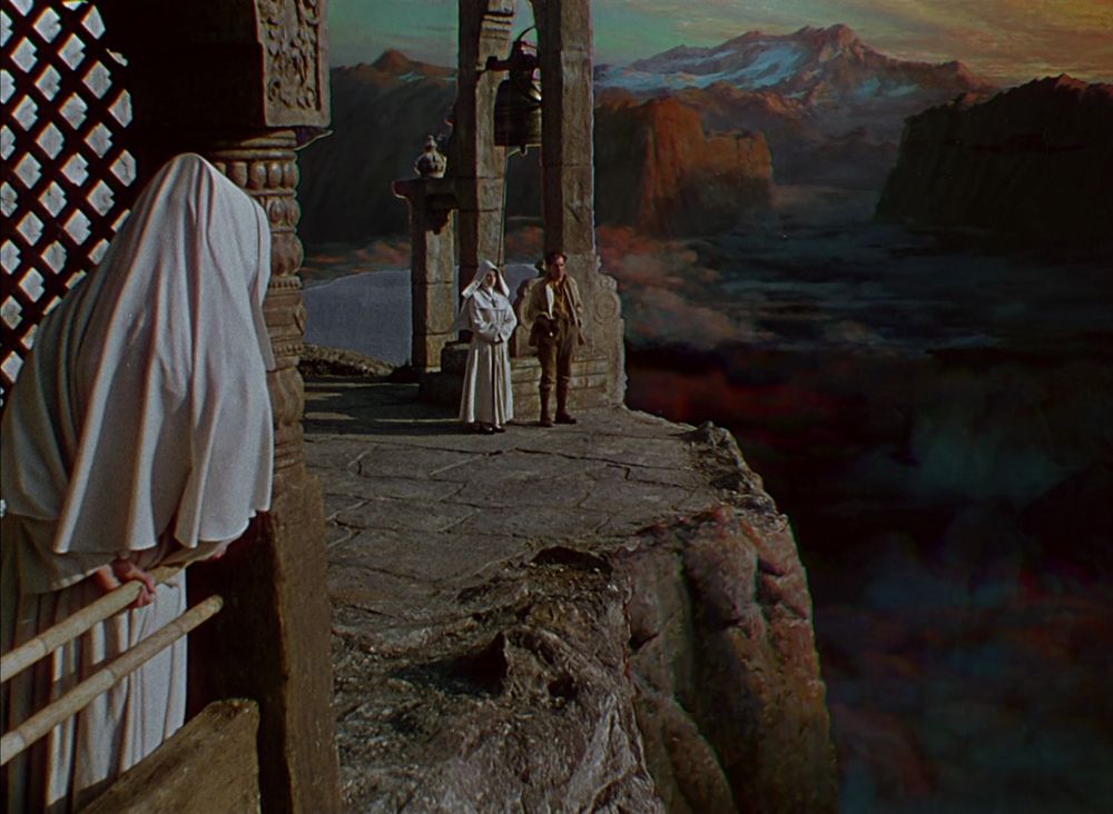 a still from Black Narcissus (1947). a nun in white robes is talking to a casually dressed man in the background, while another looks on in the foreground