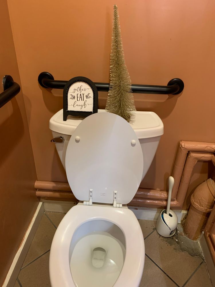 Sign over a toilet that says, “Gather, Eat, Laugh.”