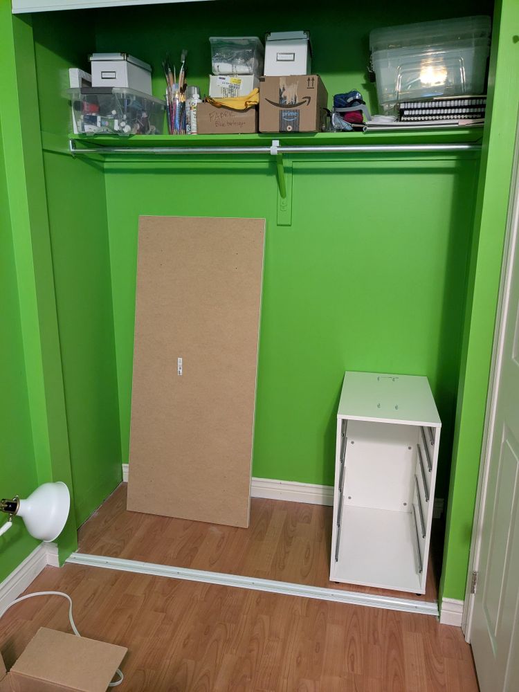 A closet painted apple green with the shell of a set of drawers and a tabletop in it.