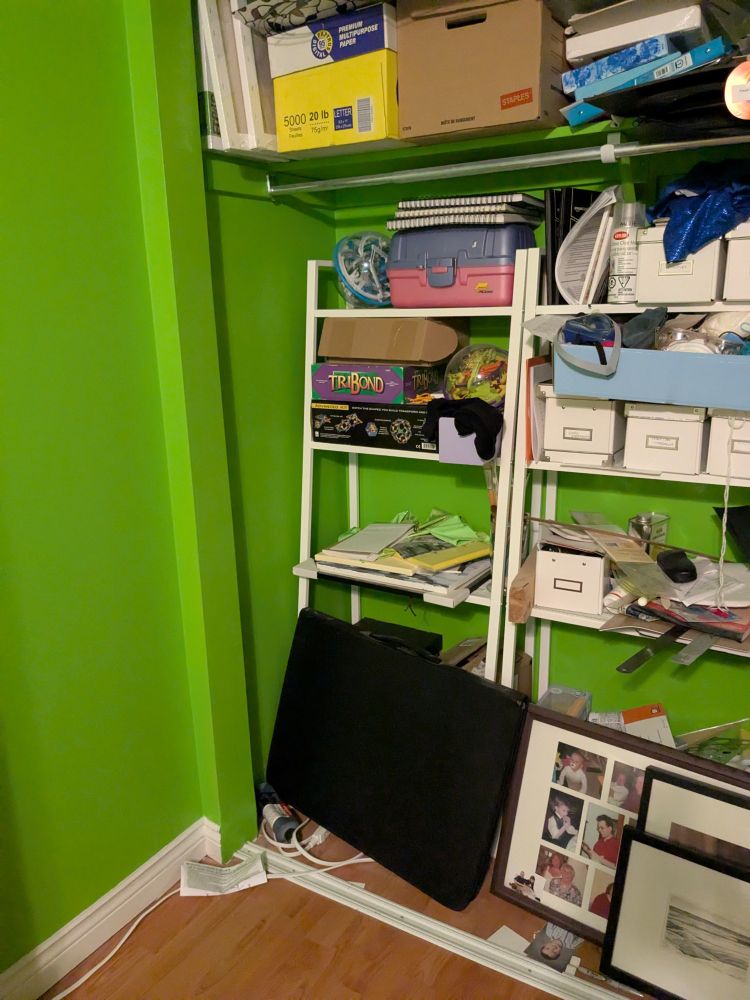 Two shelving units filled with disorganized art supplies in a closet that is painted apple green.