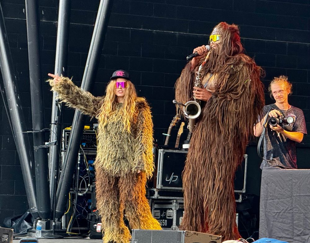 Photo of a male Sasquatch with a saxophone next to a female Sasquatch wearing a hat