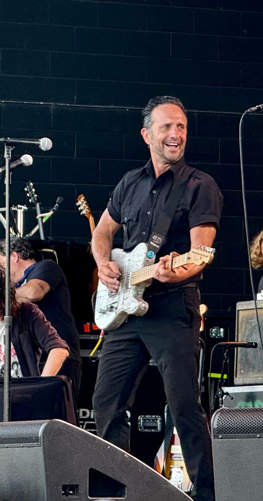 Photo of a smiling man (Ike Reilly) playing an electric guitar 