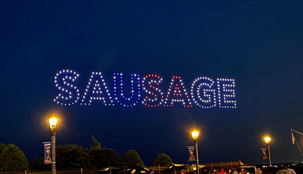 Drones spelling the word “sausage” in the evening sky. The “USA” in “sausage” is emphasized. I guess you can’t spell sausage without USA. 