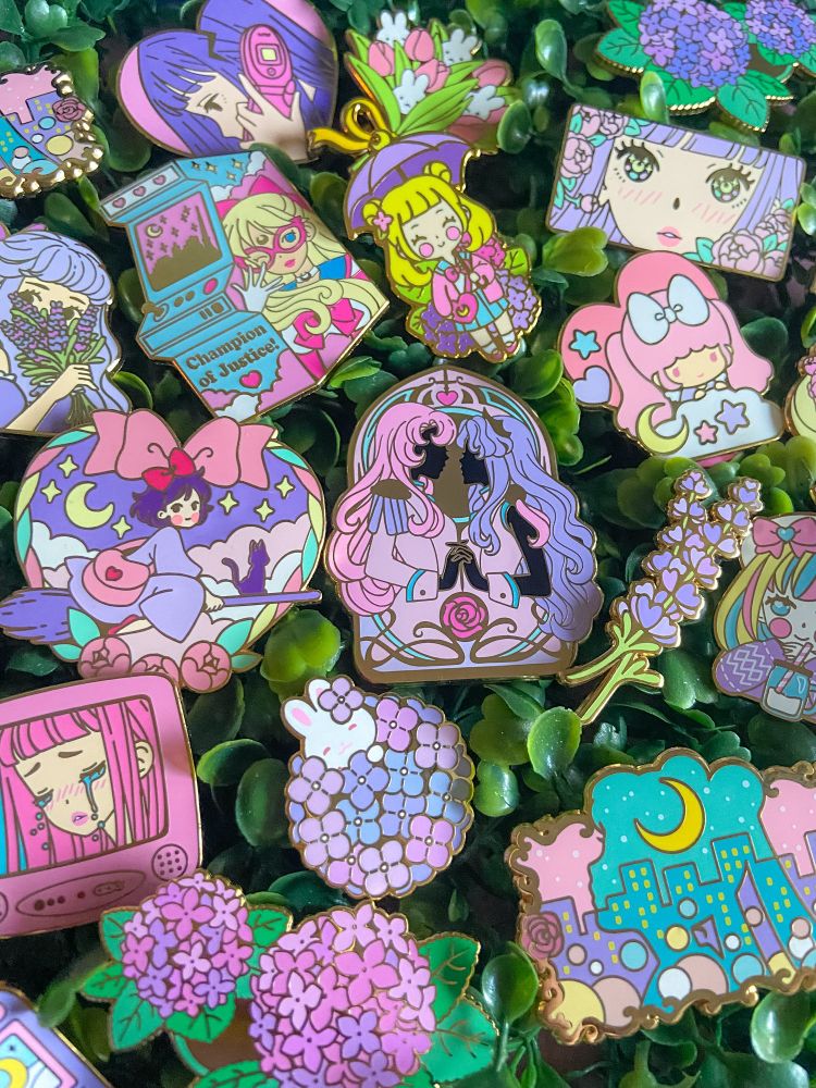 Assorted colourful enamel pins on a background of green leaves.