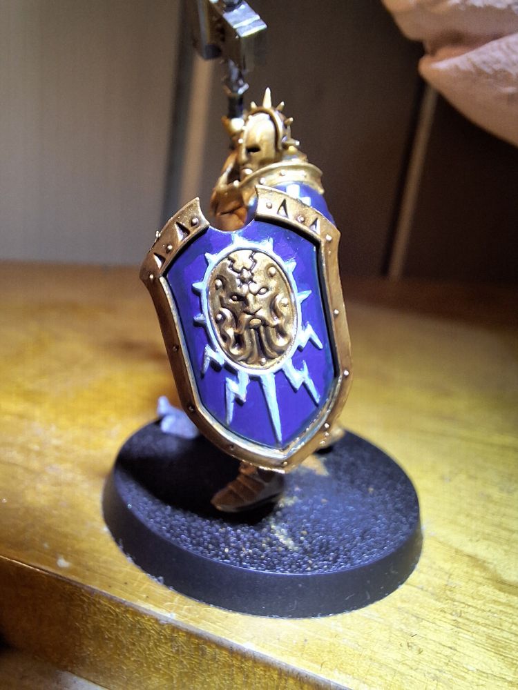 Alternate angle showing the Eternal's shield. The shield shows a golden, bearded face surrounded by light blue lightning bolts on a blue background.